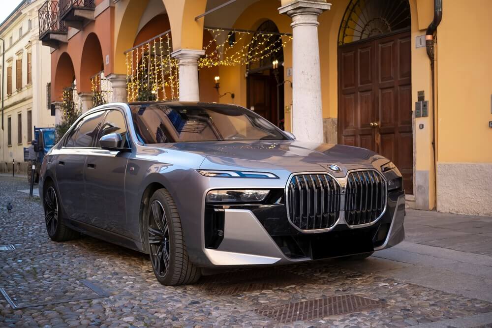 Eine elegante elektrische BMW i7 XDrive60 Limousine, die neben einem historischen Gebäude geparkt ist, demonstriert umweltfreundlichen Luxus und Automobildesign
